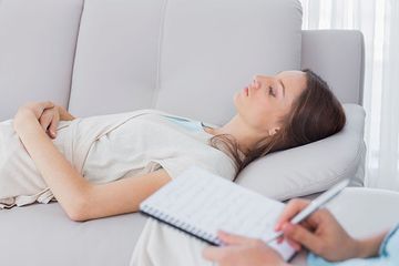 Una mujer está acostada en un sofá mientras un hombre escribe en un cuaderno.