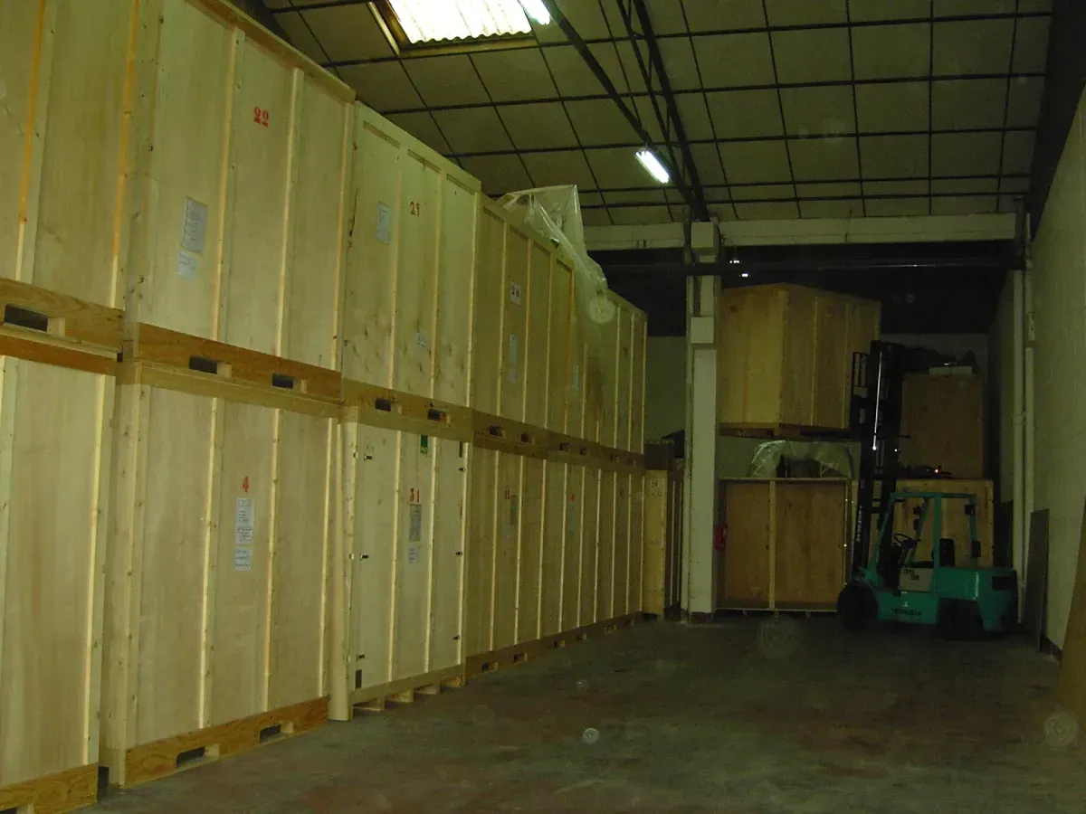 Cajas de madera apiladas en un almacén; al fondo se ve una carretilla elevadora.