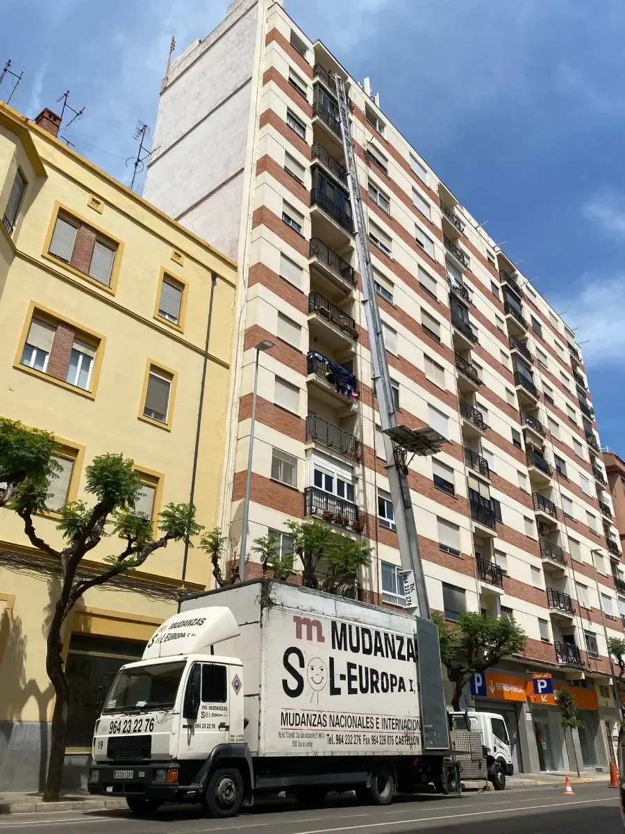 Un ascensor naranja y blanco que sube por un edificio. Obras con vallado.