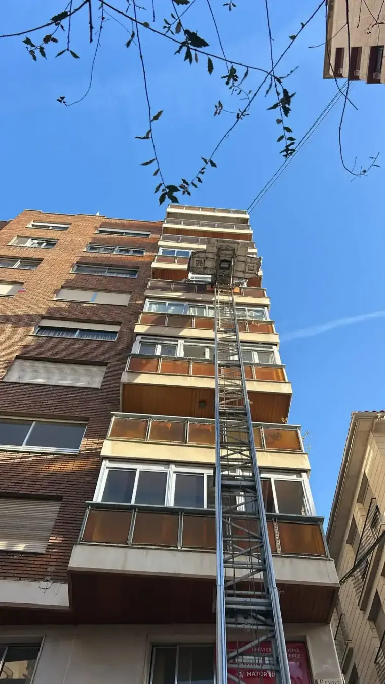 Un edificio alto de ladrillo con un ascensor que sube. Cielo azul.