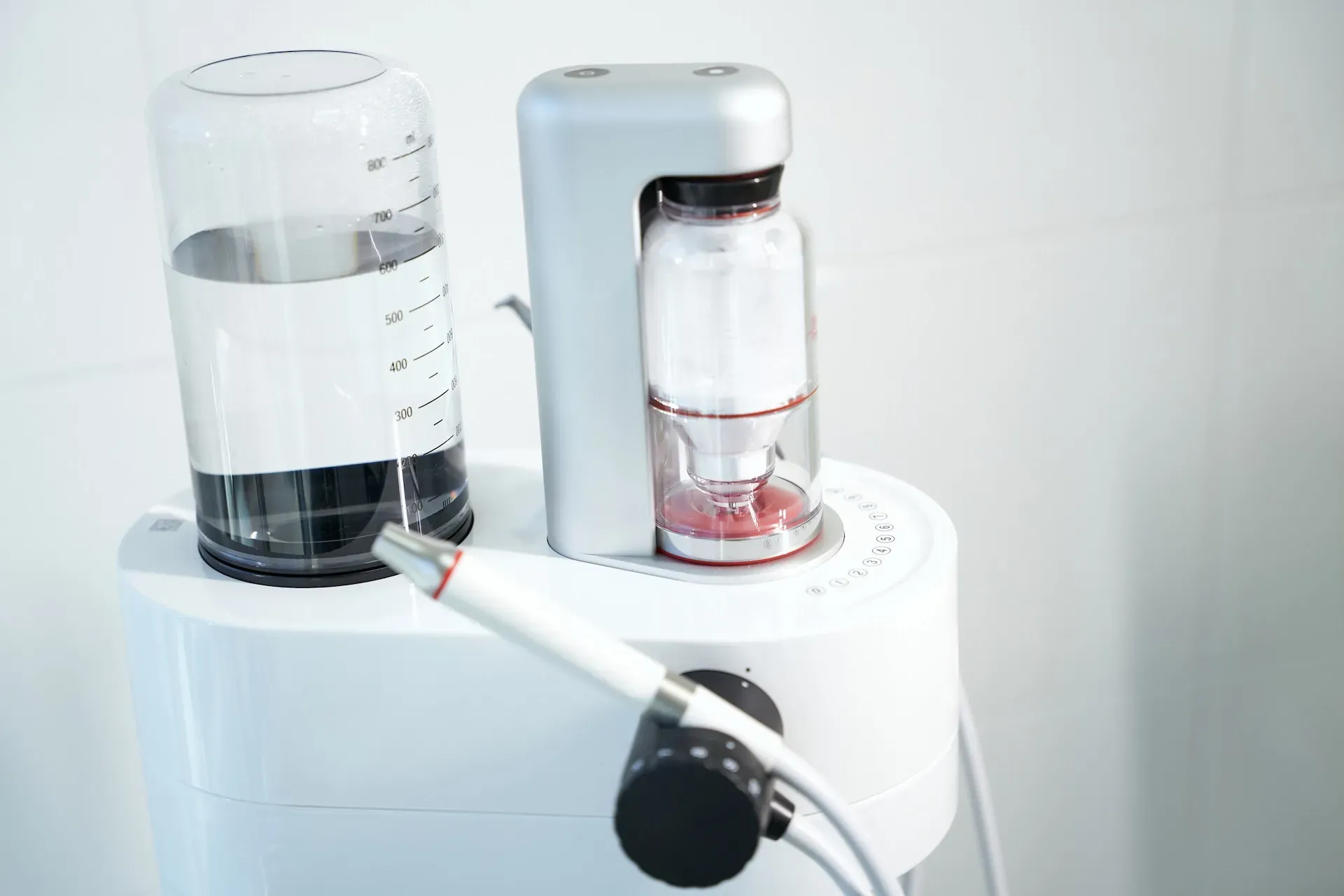 Dispositivo de limpieza dental: unidad blanca con recipientes para agua y solución transparentes y pieza de mano acoplada.