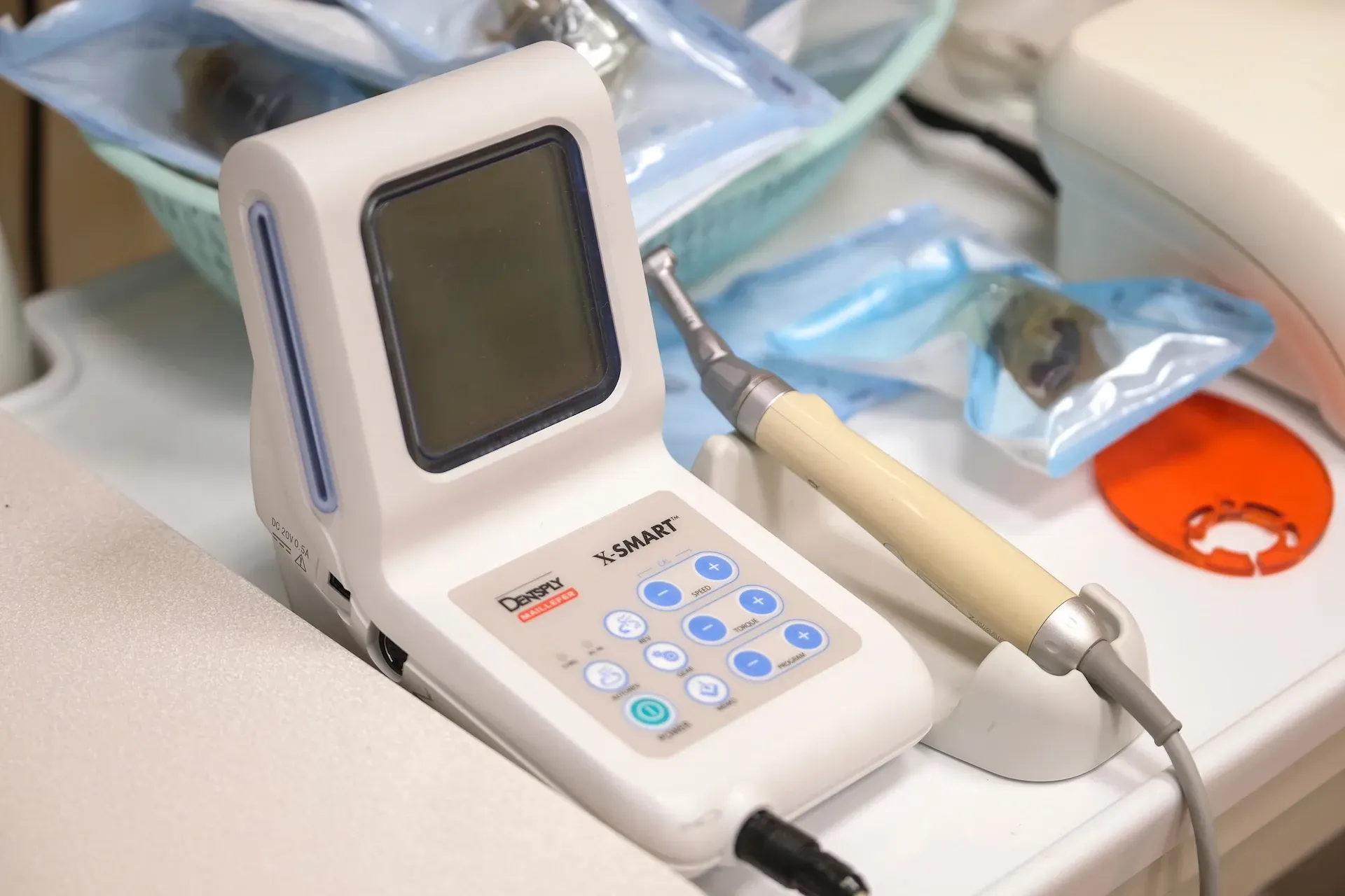 Equipo de endodoncia dental con pantalla LCD, botones azules y pieza de mano, en entorno clínico.