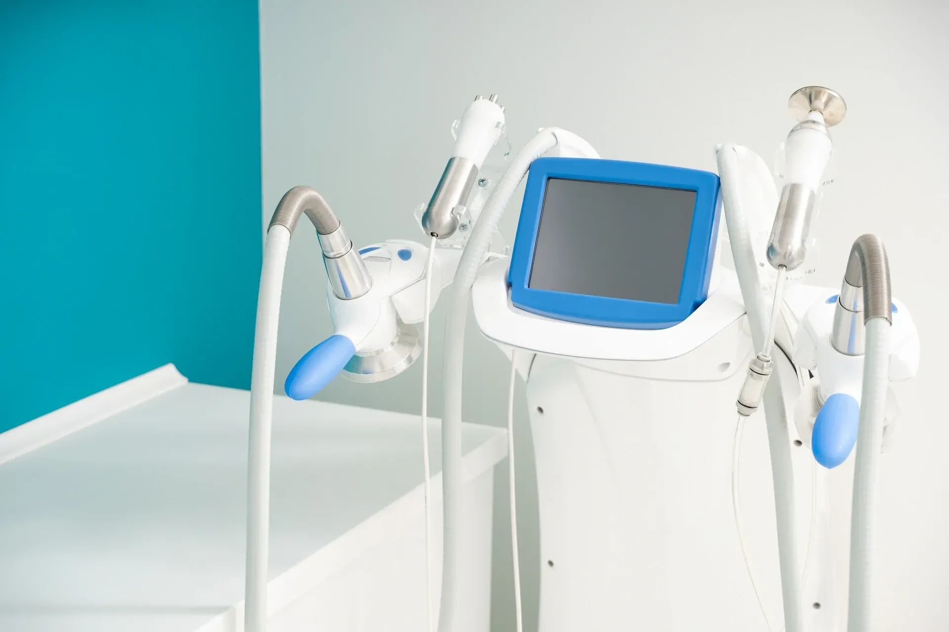 Dispositivo médico con una pantalla azul y varios aplicadores adjuntos, en un entorno médico.