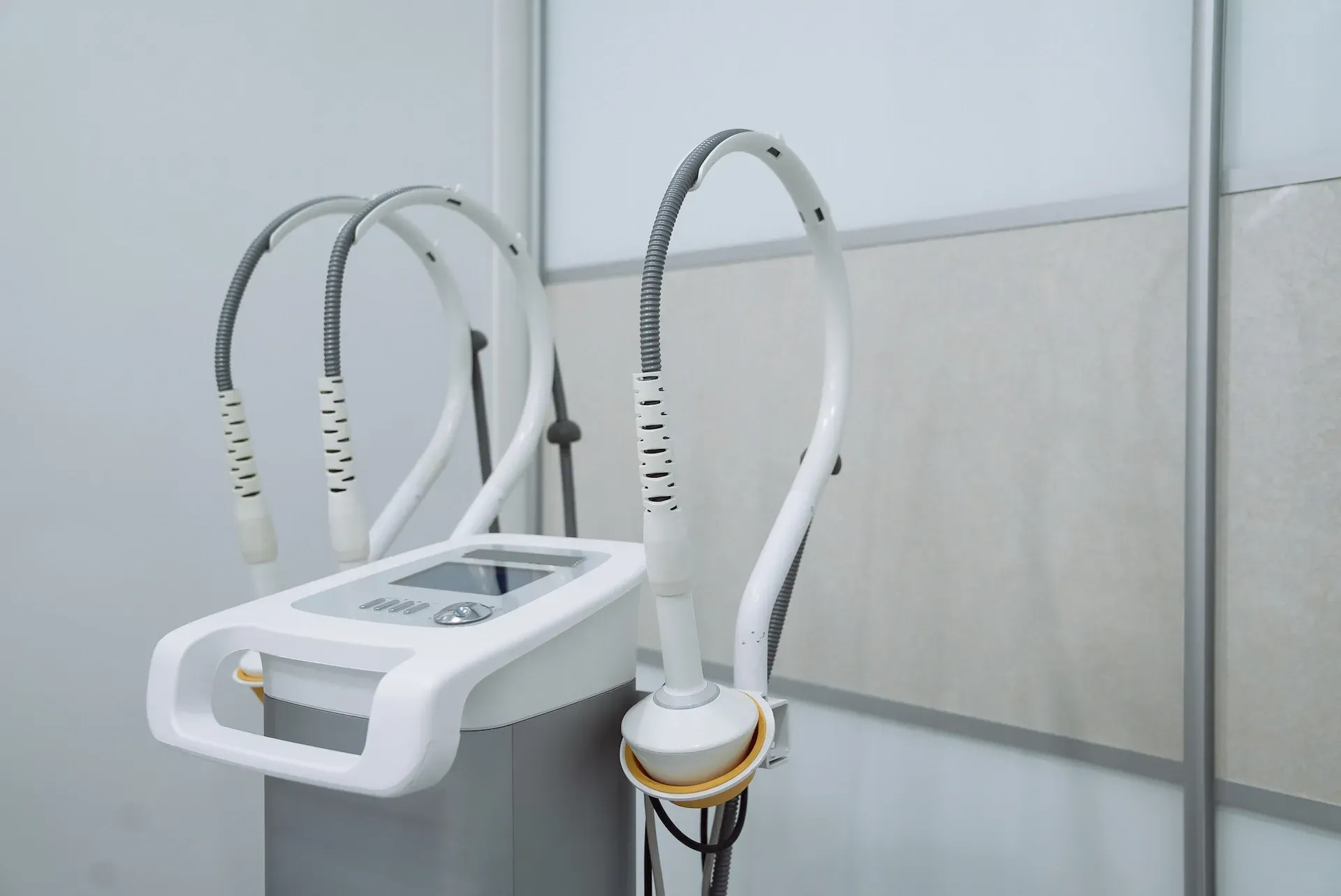 Máquina médica blanca con brazos curvos y panel de control, en una habitación con pared blanca.
