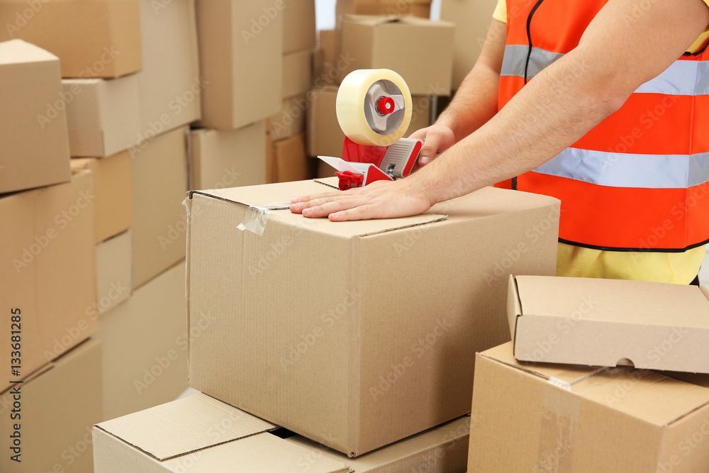 Ein Mann verklebt in einem Lagerhaus einen Karton mit Klebeband.