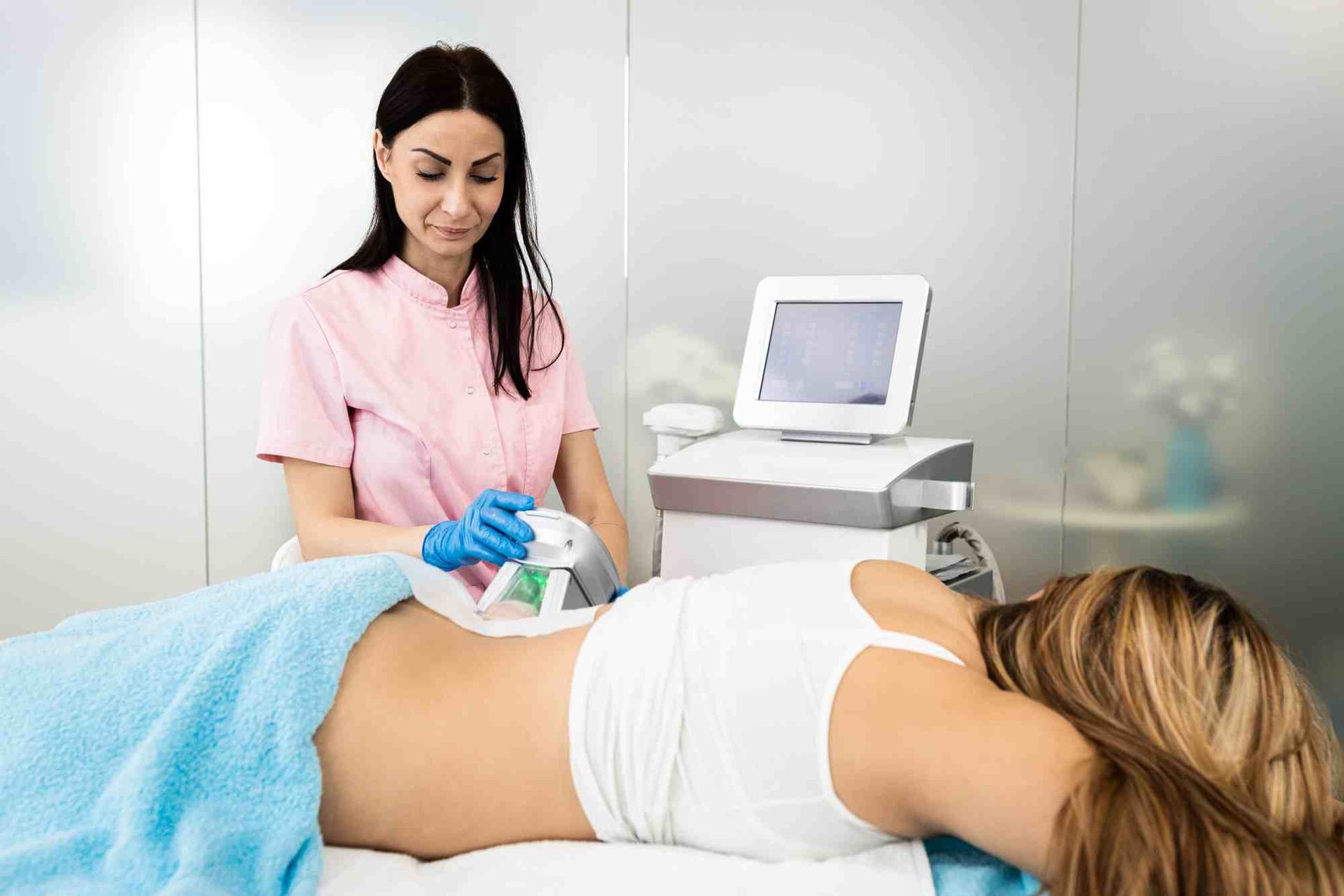 Eine Frau in rosa OP-Kleidung benutzt eine Ultraschallsonde an einem Patienten, der auf einer Behandlungsliege liegt.