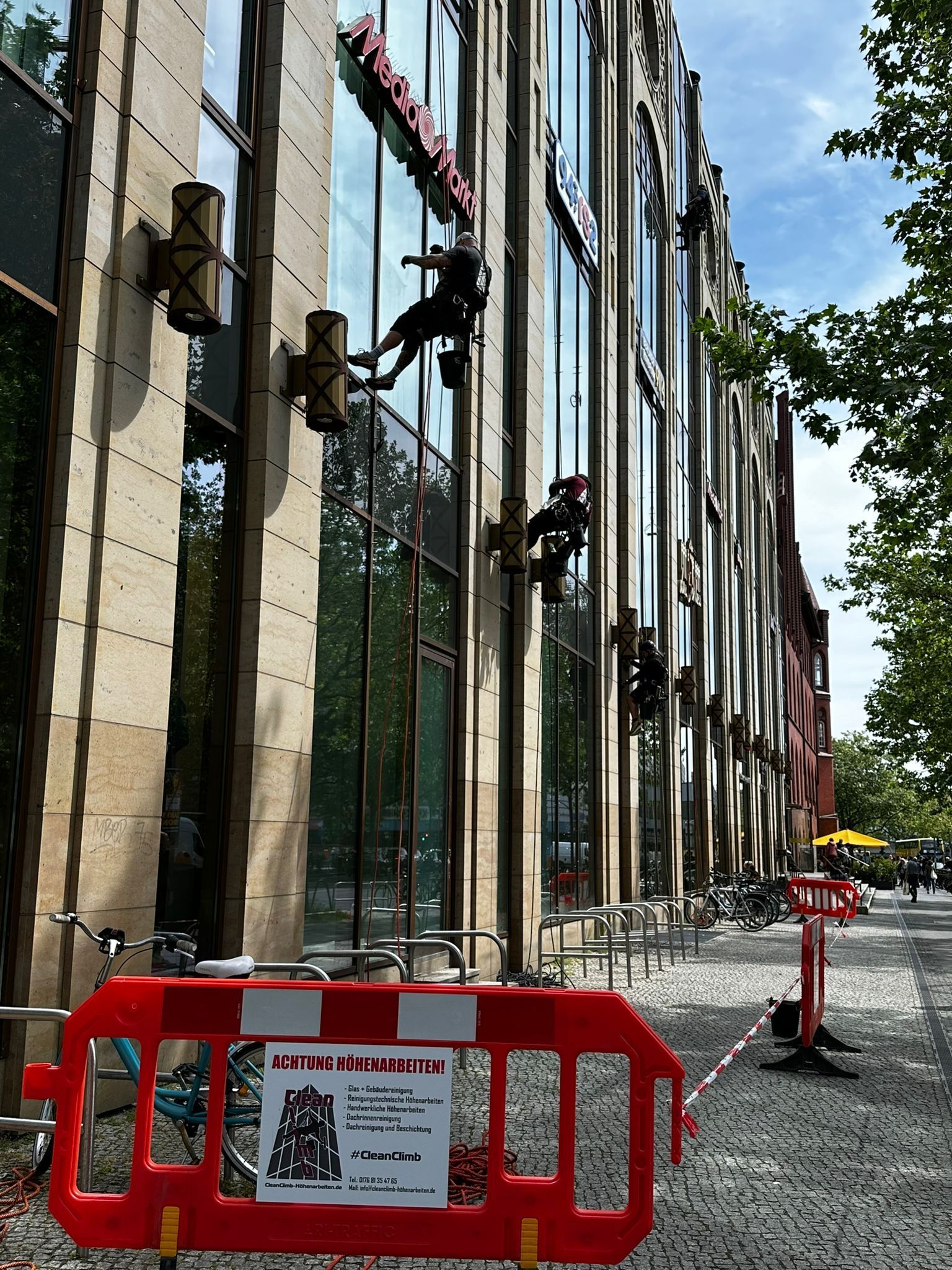 Fenster eines hohen Gebäudes werden von außen, in der Luft hängend, gereinigt