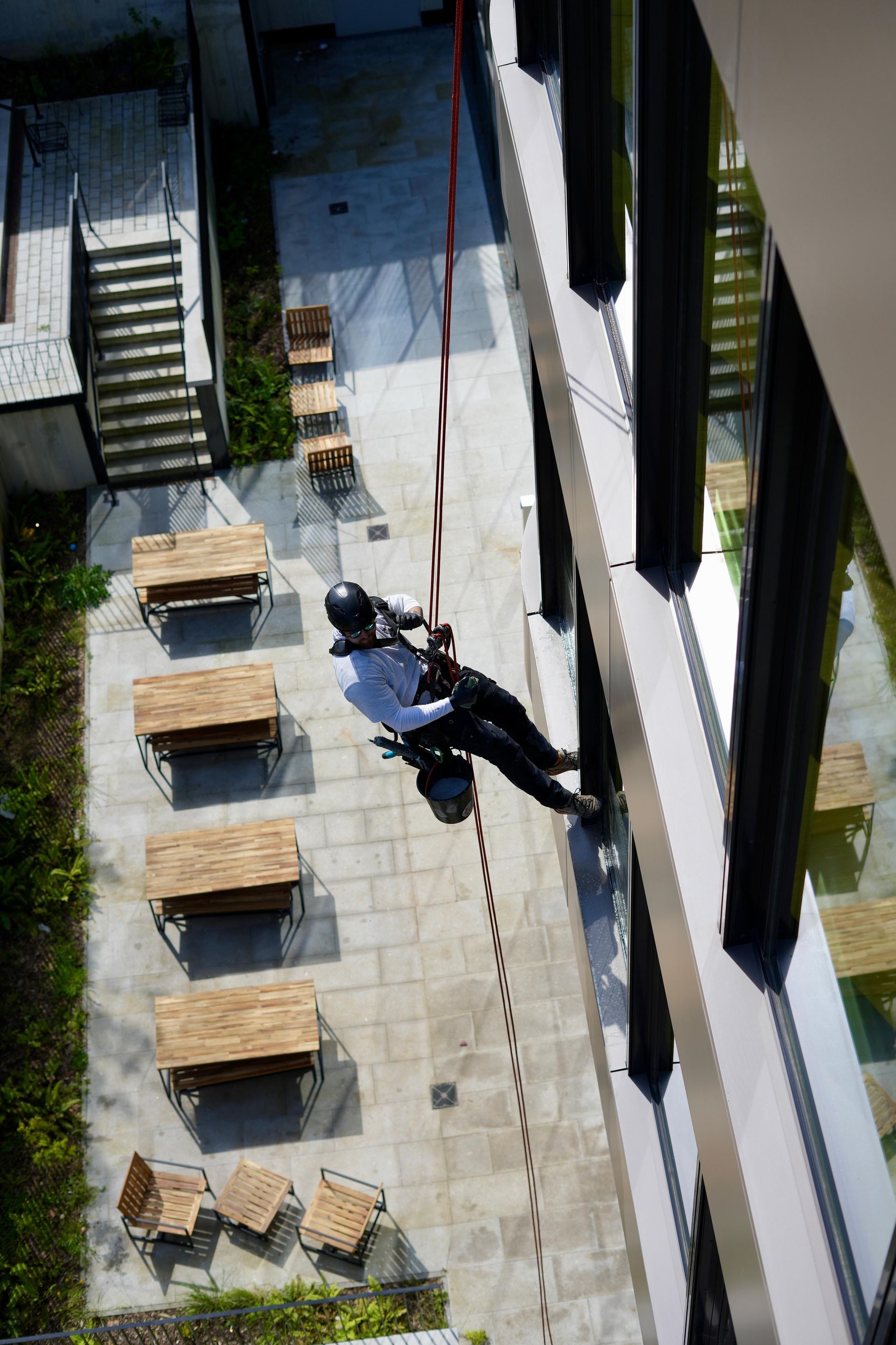 Mitarbeiter hängt mit einem Seil befestigt an einem Gebäude und reinigt die Fenster