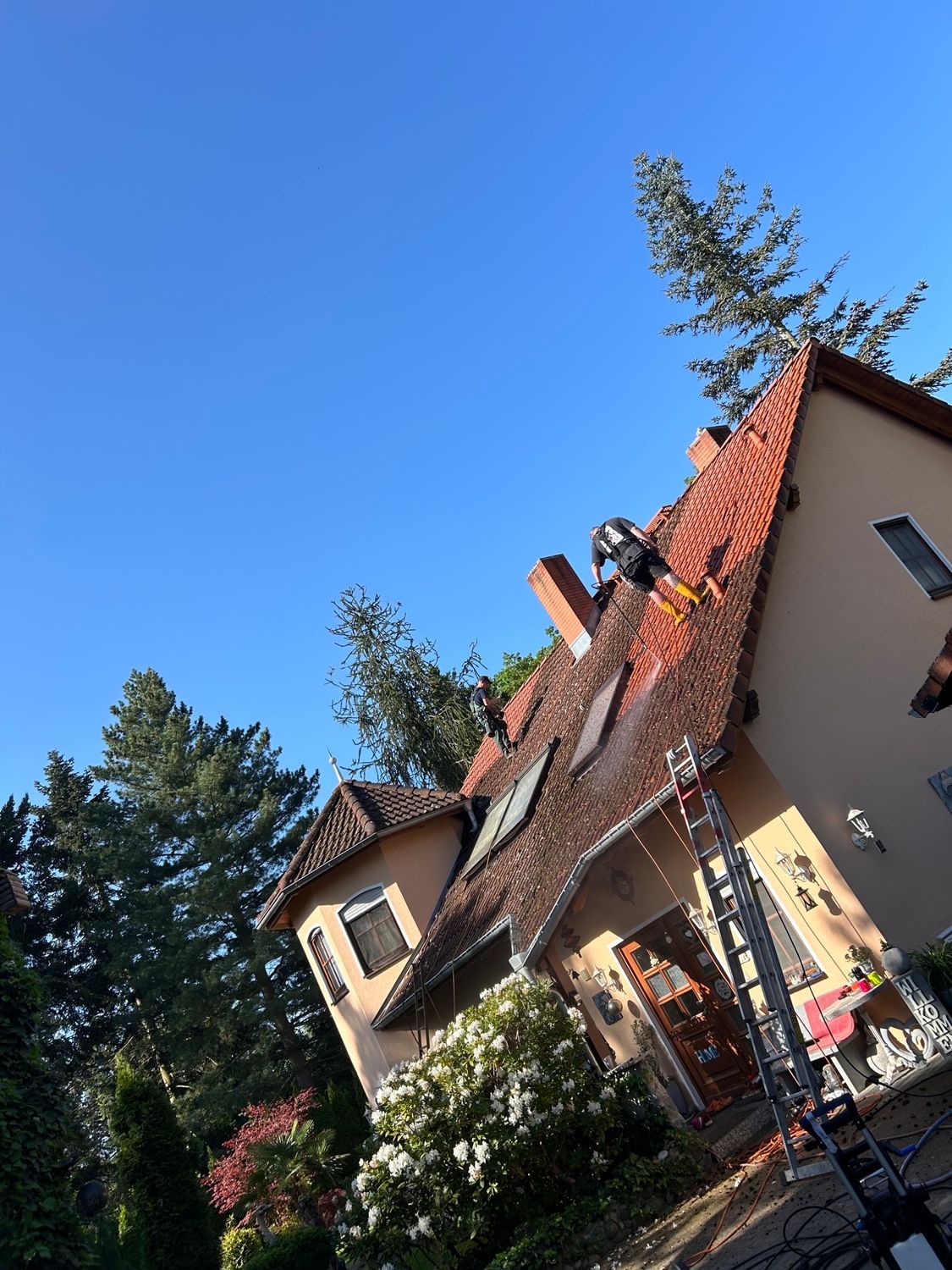 Höhenreinigung: Mitarbeiter steht auf dem Dach eines Hauses und reinigt die Schindeln