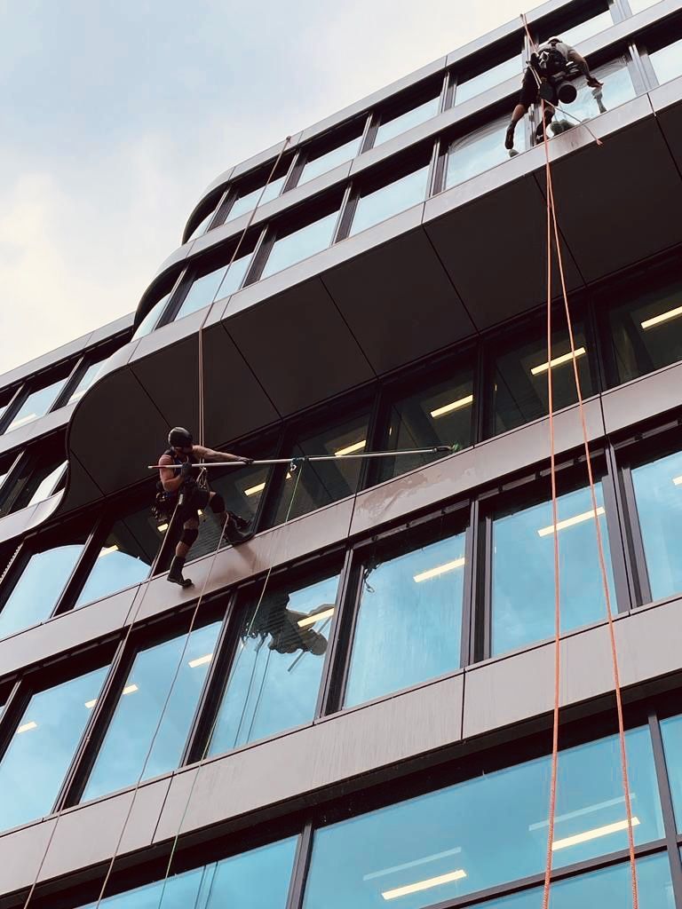 Mitarbeiter hängt an der Seite eines Gebäudes und reinigt die Fenster von außen