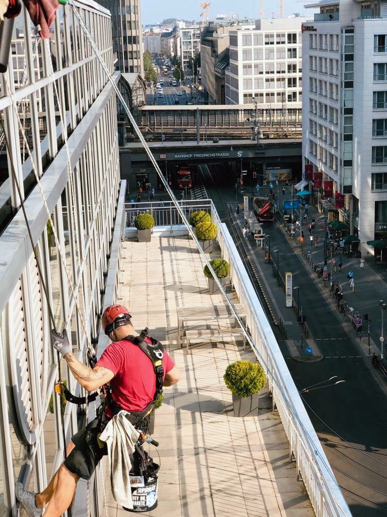 Mitarbeiter hängt an der Fassade eines Berliner Gebäudes und reinigt die Fenster