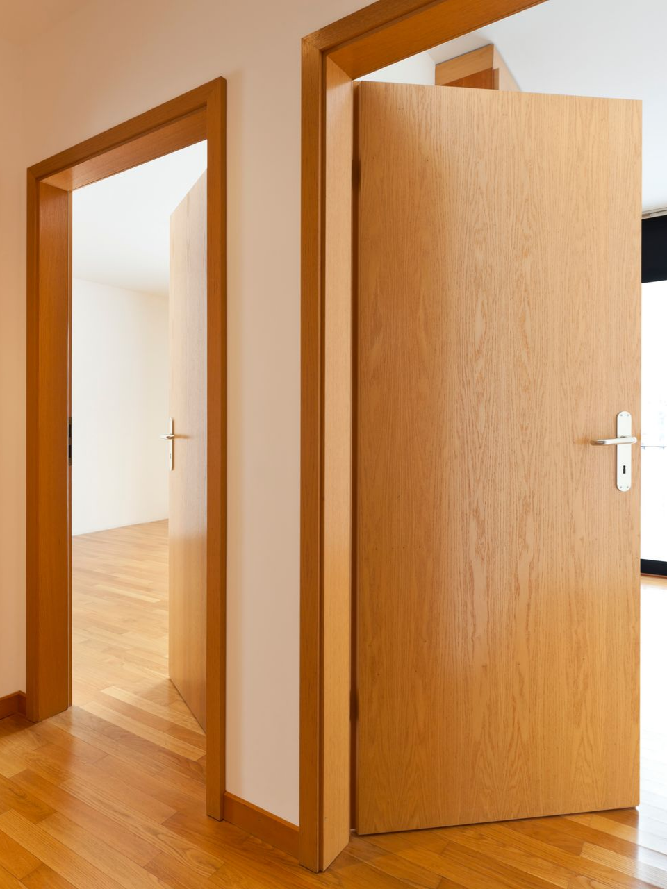 Deux portes en bois ouvertes dans un couloir, avec une pièce baignée de lumière visible en arrière-plan.