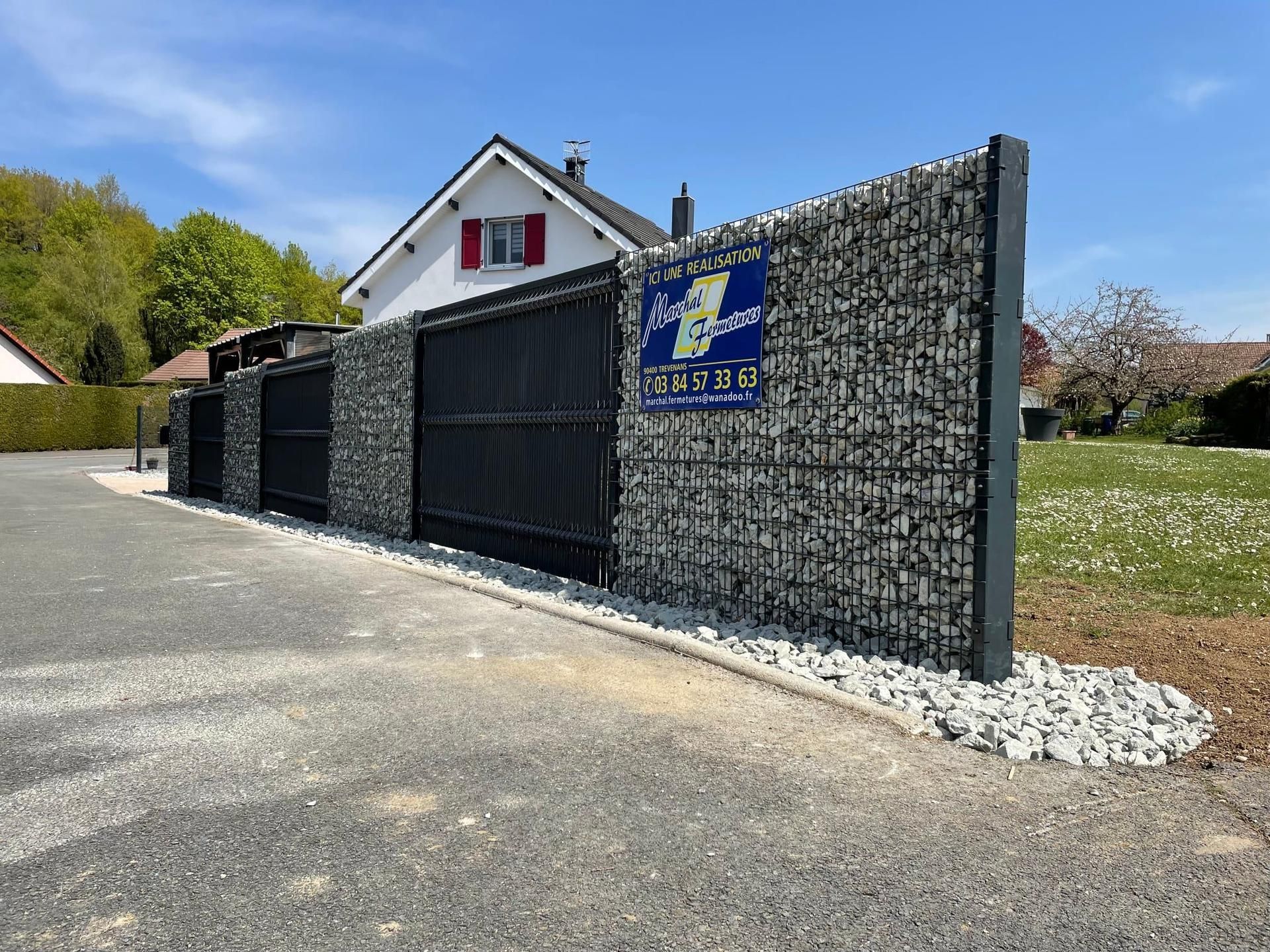 Clôture en gabions et en métal avec portail devant une maison.