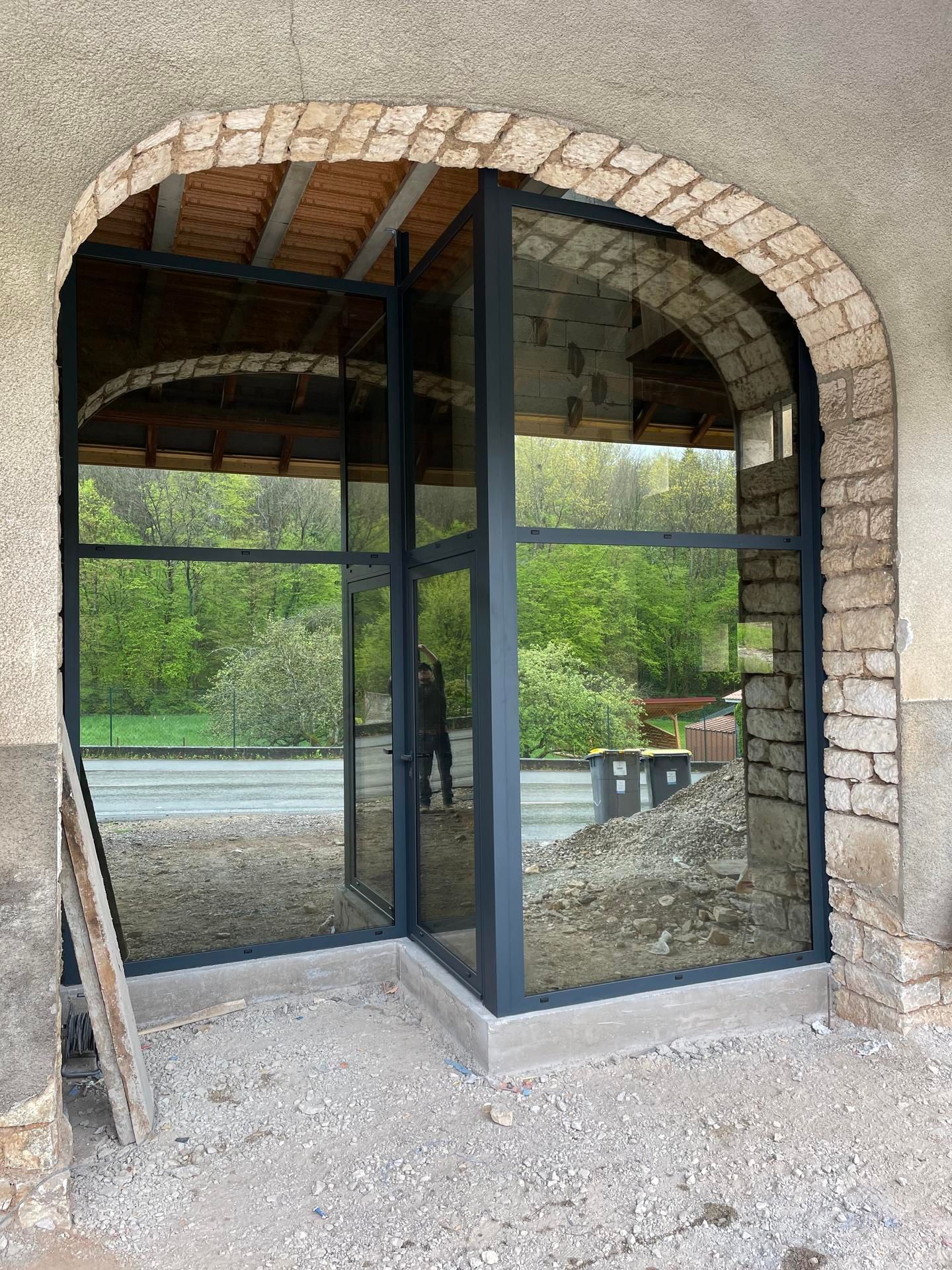 Porte vitrée et panneaux latéraux à l'intérieur d'une arche en briques ; une personne se reflète dans le verre.