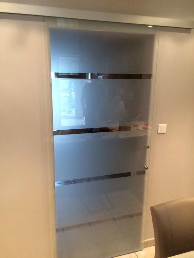 Porte coulissante en verre dépoli à barres horizontales argentées, dans une pièce aux murs beiges.