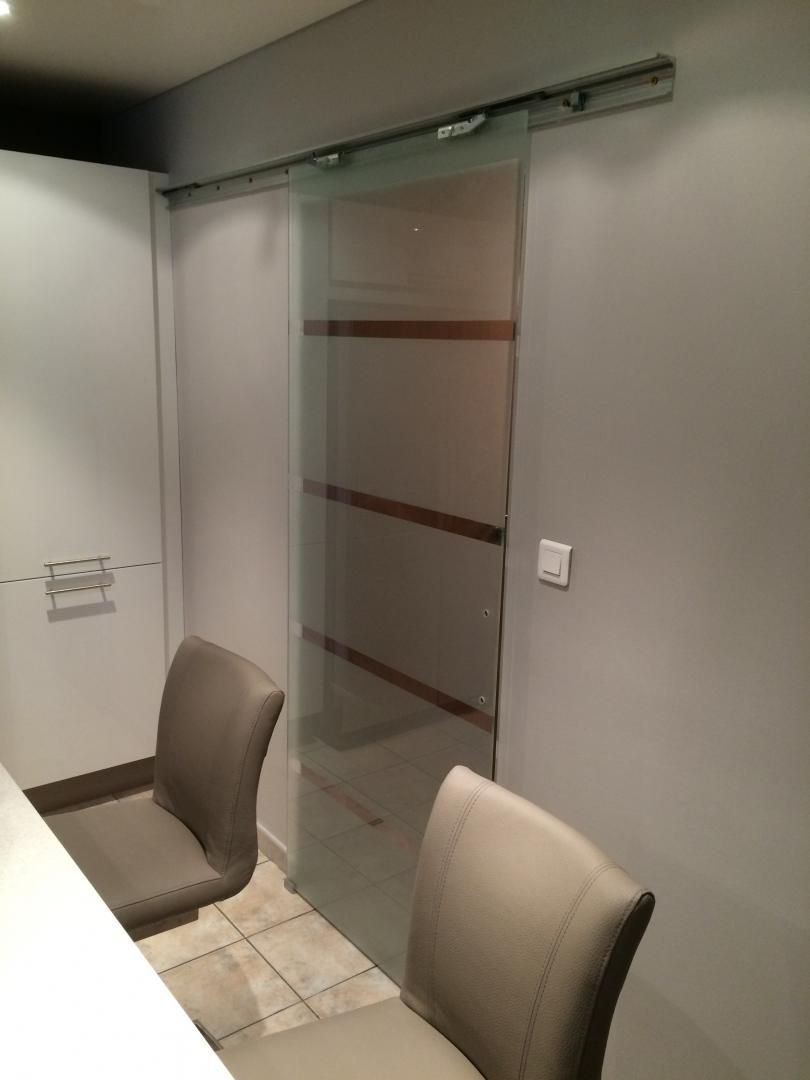 Porte coulissante en verre avec accents de bois, montée sur un rail, murs gris, deux chaises.