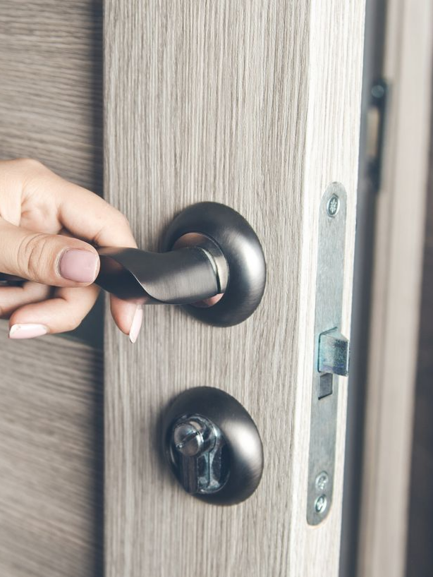 Une main qui tourne une poignée de porte noire sur une porte en bois gris.