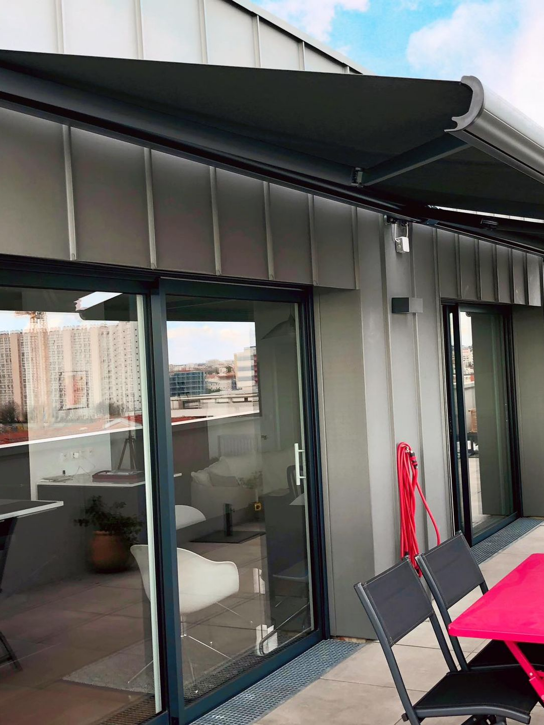 Un store banne gris s'étendait au-dessus d'un balcon à portes vitrées, donnant sur la ville.