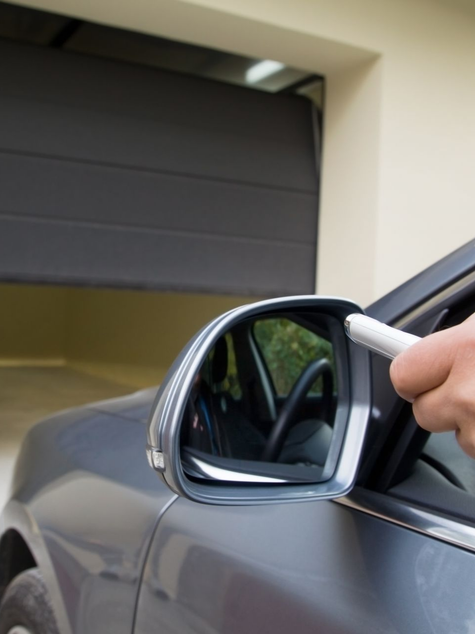 Voiture grise près d'un garage, main tenant la télécommande pour ouvrir la porte de garage.