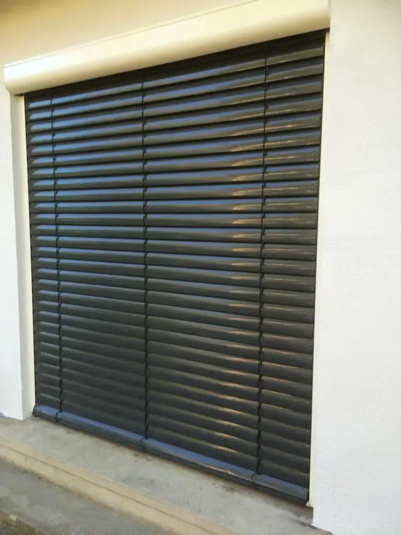 Volet roulant gris foncé fermé sur un bâtiment blanc, assurant sécurité et protection solaire.