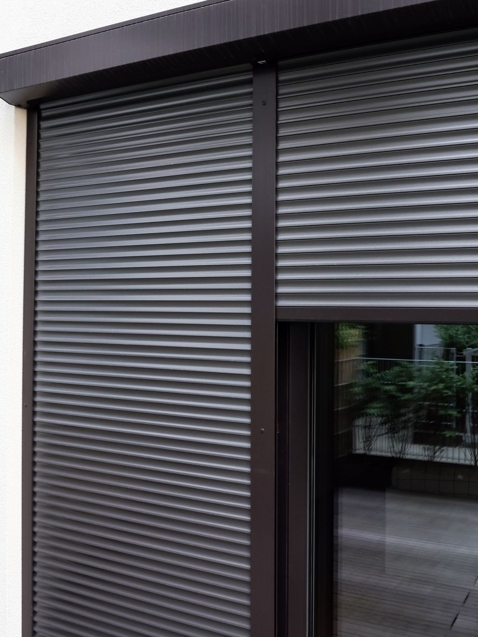 Volet roulant foncé recouvrant partiellement une fenêtre. Vue extérieure d'un bâtiment avec le volet fermé.
