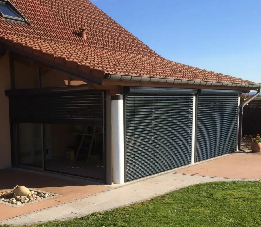 Volets ou stores gris foncé masquant les fenêtres d'une véranda par une journée ensoleillée.
