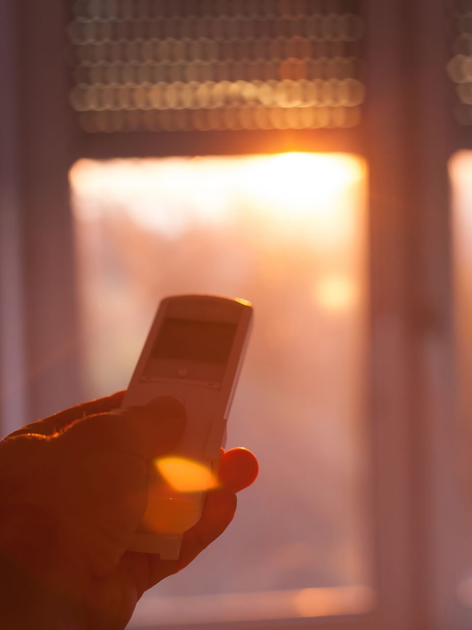 Une main tenant une télécommande et silhouette sur la lumière vive du soleil filtrant à travers une fenêtre.