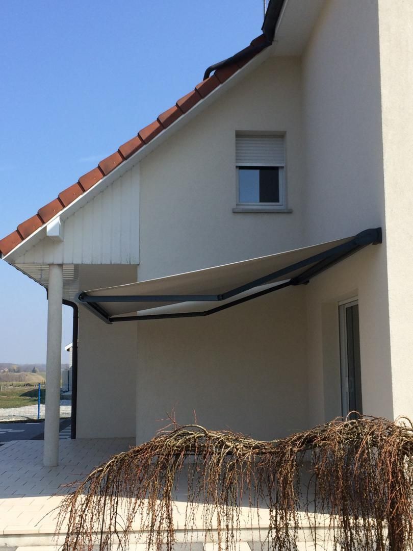 Extérieur d'une maison beige avec un auvent et une fenêtre, donnant sur des branches au premier plan.