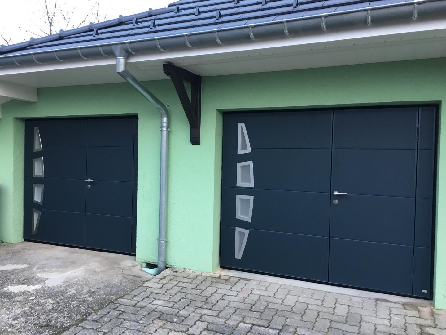 Deux portes de garage bleu foncé sur un bâtiment au toit gris.