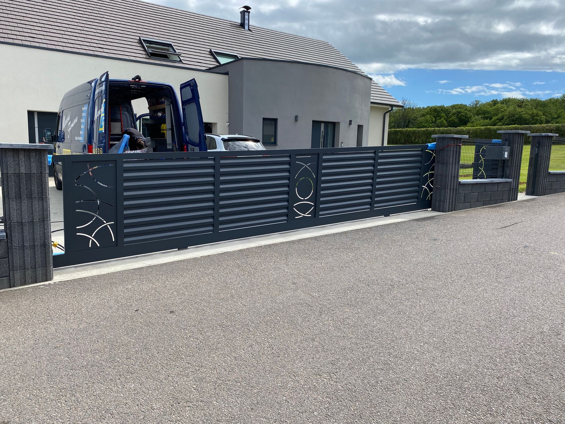 Clôture métallique grise avec découpes décoratives devant une maison moderne