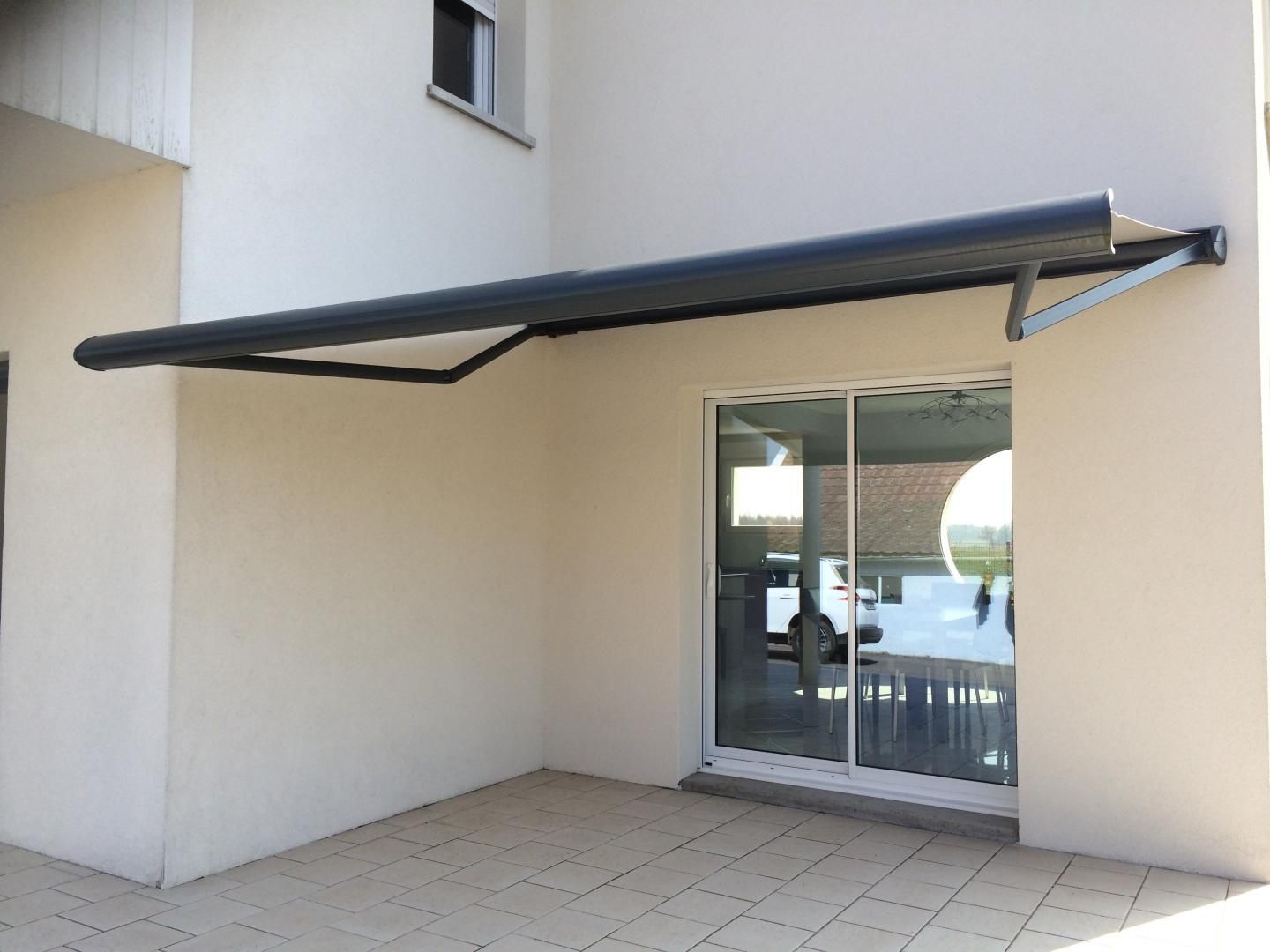 Store à coffre gris au-dessus d'une baie vitrée sur un bâtiment en stuc.