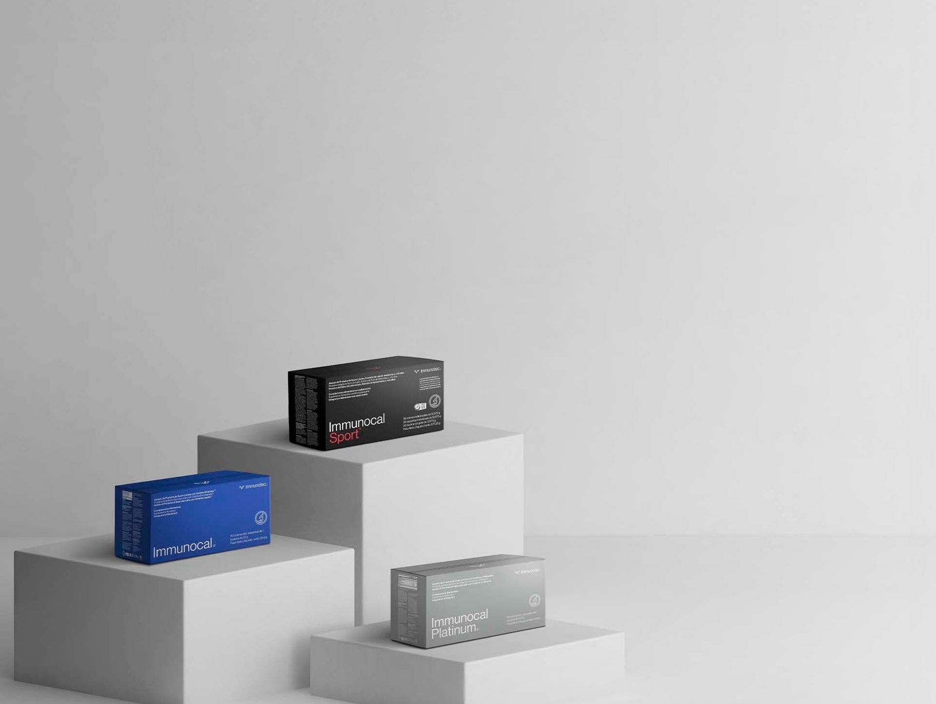 Tres cajas de productos en azul, negro y gris mostradas en plataformas geométricas blancas sobre un fondo blanco.