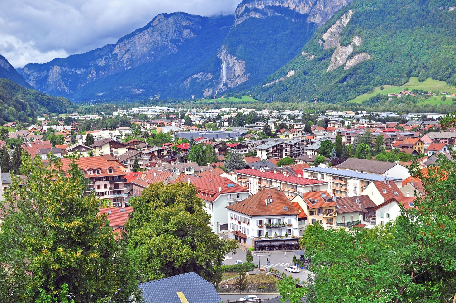 Ville aux toits rouges, nichée au pied de montagnes verdoyantes sous un ciel bleu nuageux.