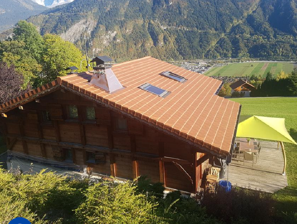 Cabane en bois au toit orange, perchée à flanc de montagne, surplombant une vallée et des sommets lointains.