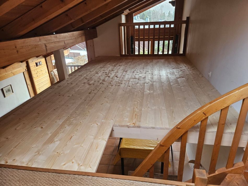 Grenier vide avec plancher en bois, plafond mansardé et rampe d'escalier au premier plan.