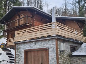 Chalet enneigé avec extérieur en pierre et en bois, terrasse enveloppante et escalier dans un cadre boisé à flanc de colline