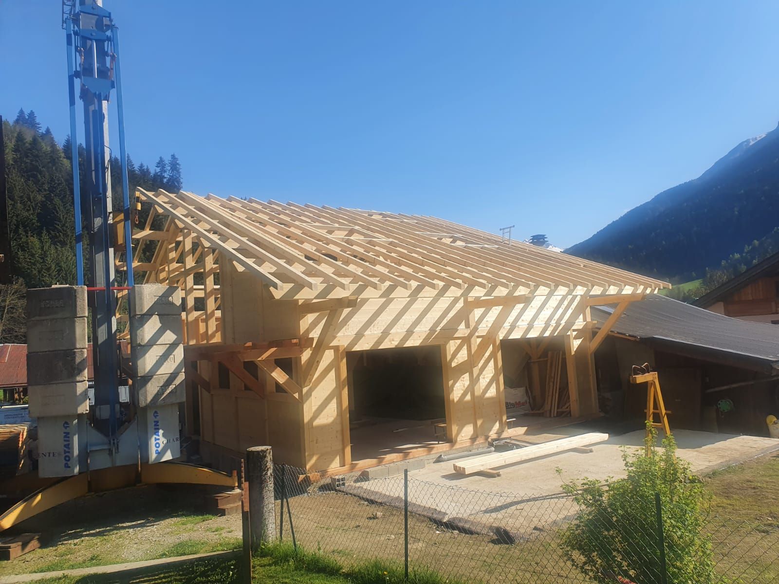 Maison à ossature en bois en construction avec charpente apparente et fondations en béton dans un environnement montagneux