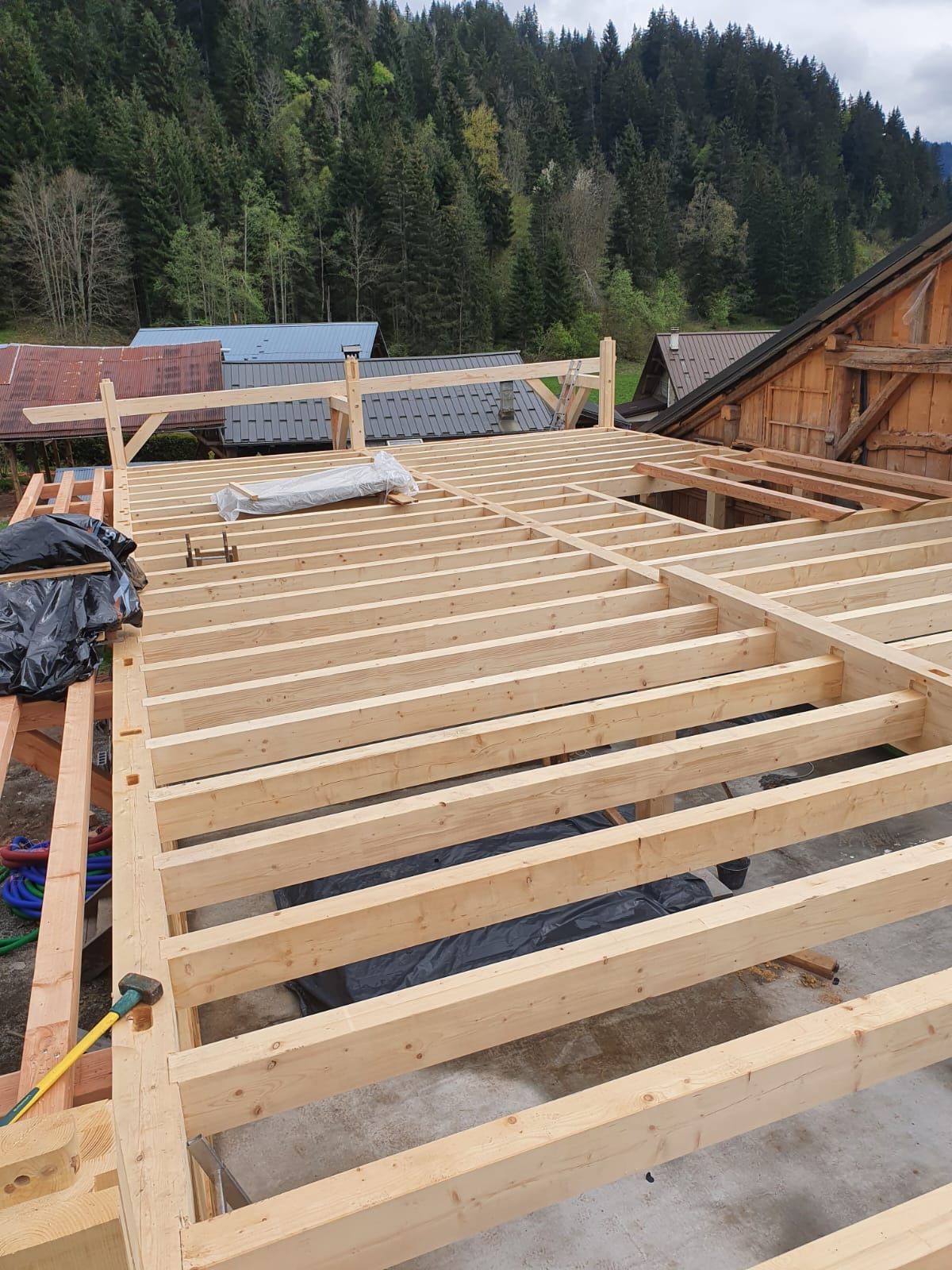 Charpente en bois d'une maison en construction, avec des montagnes boisées en arrière-plan.