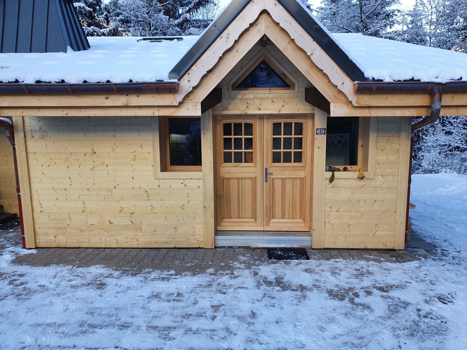 Cabane en bois enneigée avec un toit pointu et des portes doubles