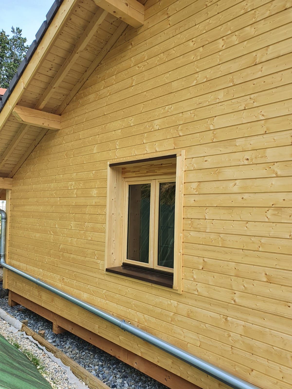 Maison en bois avec une petite fenêtre et un toit en pente sur fondations en gravier