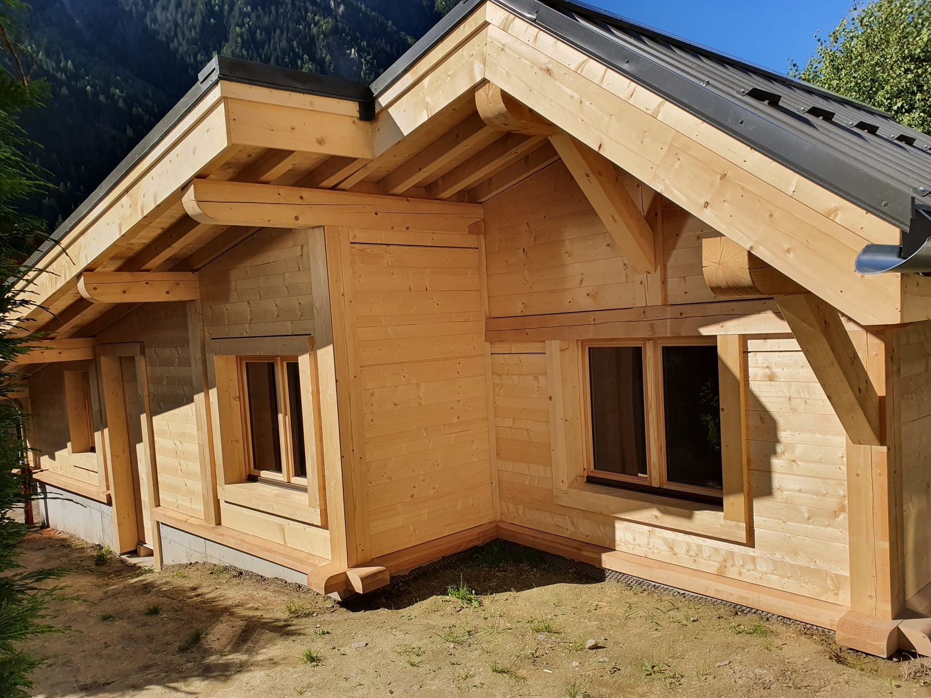 Maison en bois en construction avec poutres apparentes et murs inachevés dans une cour ensoleillée