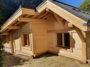 Maison en bois en construction avec poutres apparentes et murs inachevés dans une cour ensoleillée