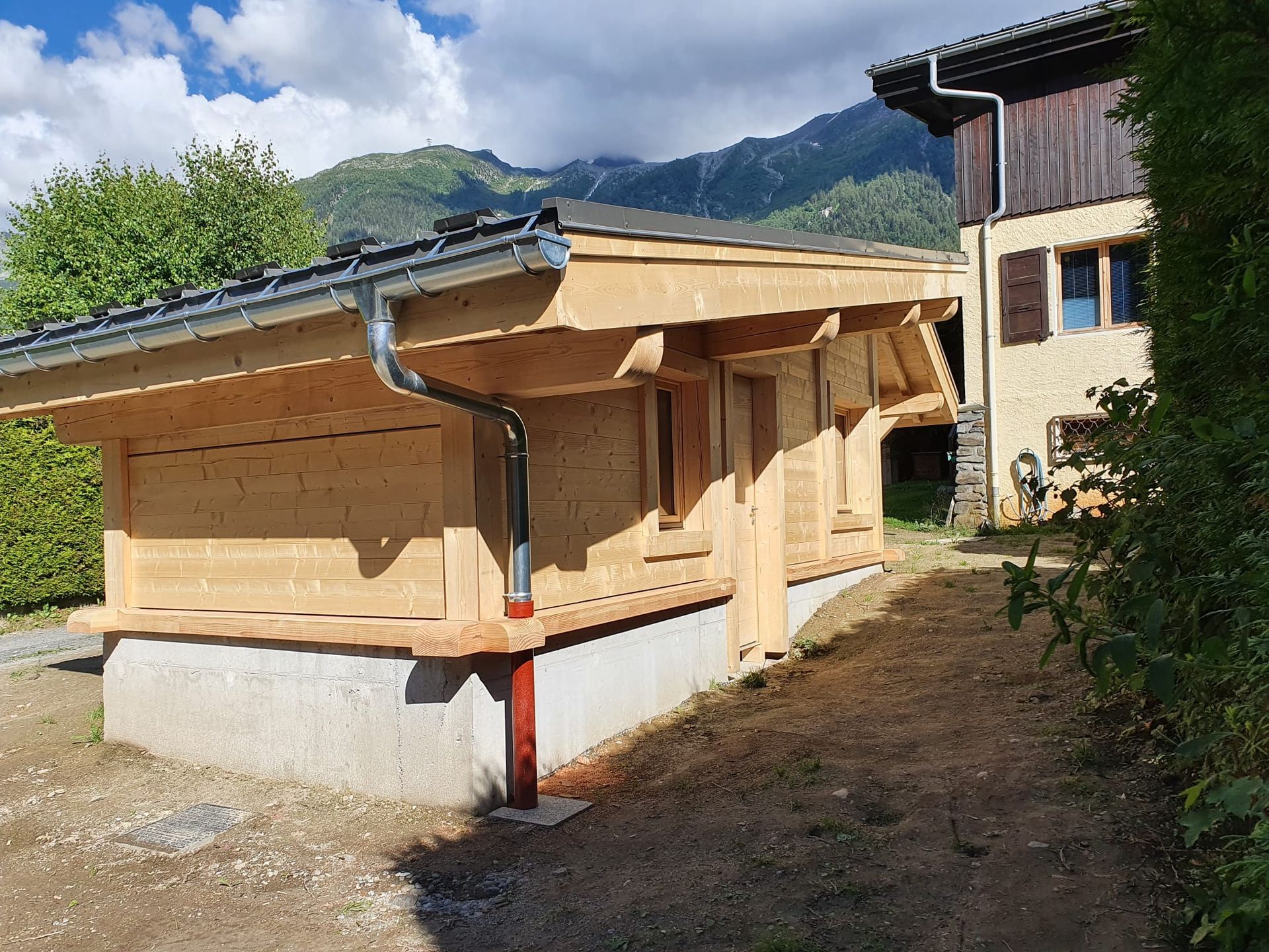 Cabane en bois en construction avec un toit en pente et des fondations en béton dans une cour rurale