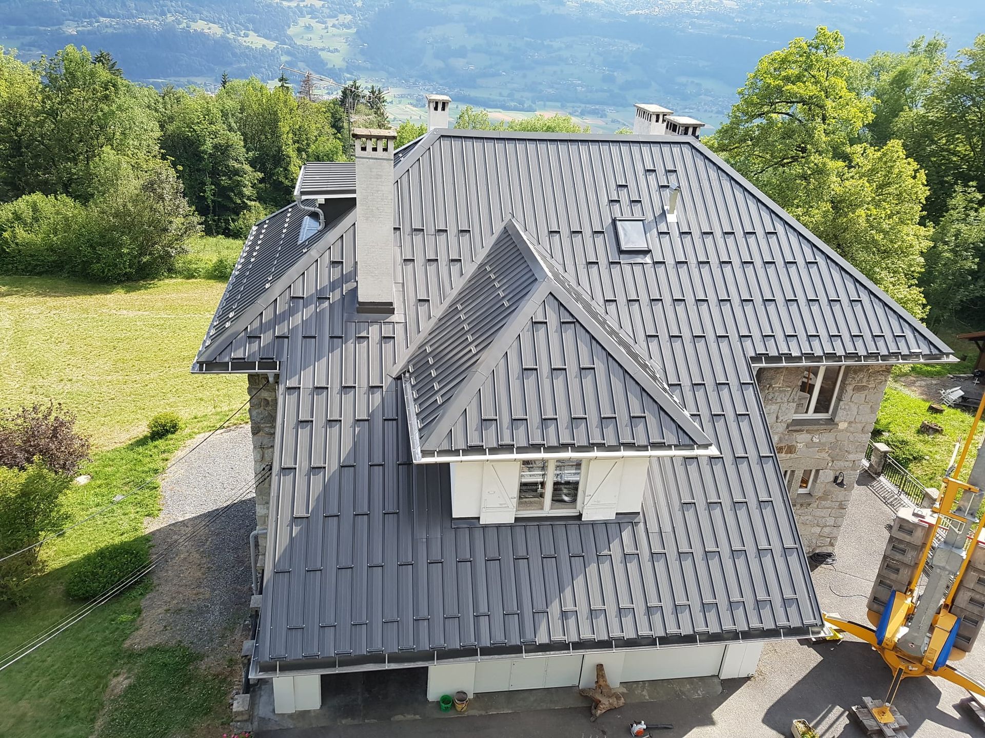 Maison avec toit en métal gris donnant sur une colline verdoyante et des montagnes