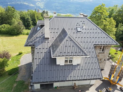 Maison avec toit en métal gris donnant sur une colline verdoyante et des montagnes