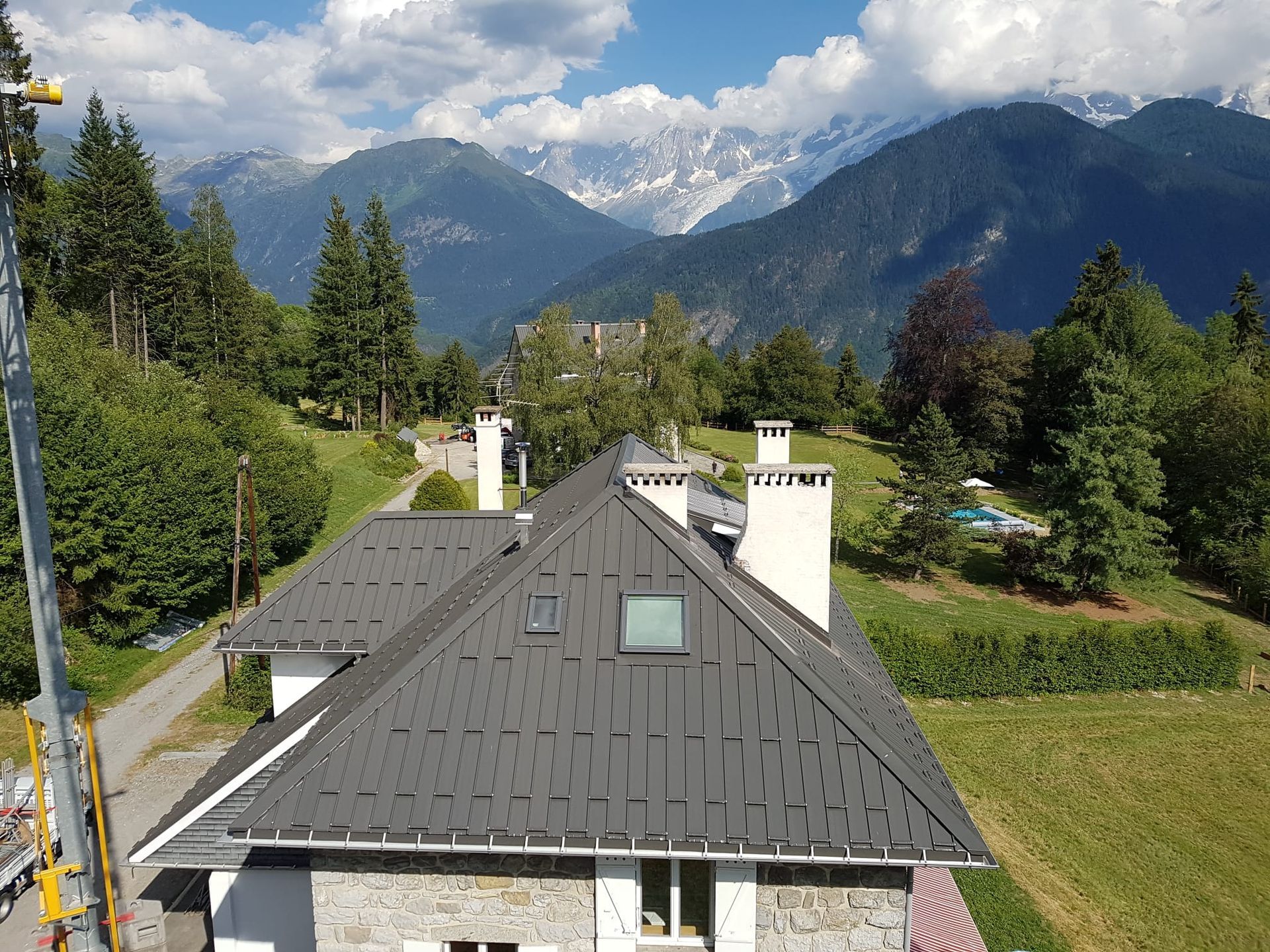 Toits d'une maison de montagne avec des pins et des nuages au-dessus des montagnes lointaines
