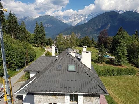 Toit de maison de montagne avec des arbres et des sommets enneigés sous un ciel nuageux