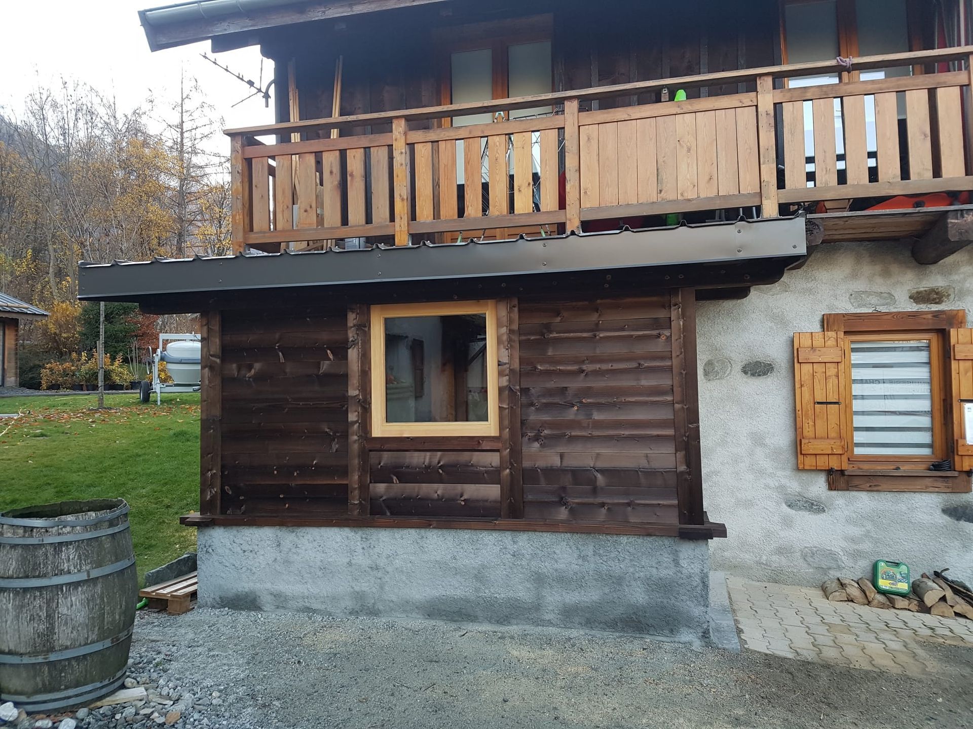 Maison rustique en bois de deux étages avec balcon, fenêtres à volets et soubassement en pierre dans un cadre rural