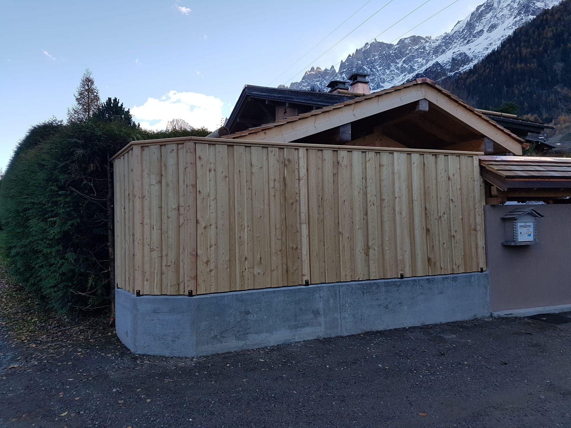 Une clôture en bois entoure une petite maison avec des montagnes en arrière-plan.