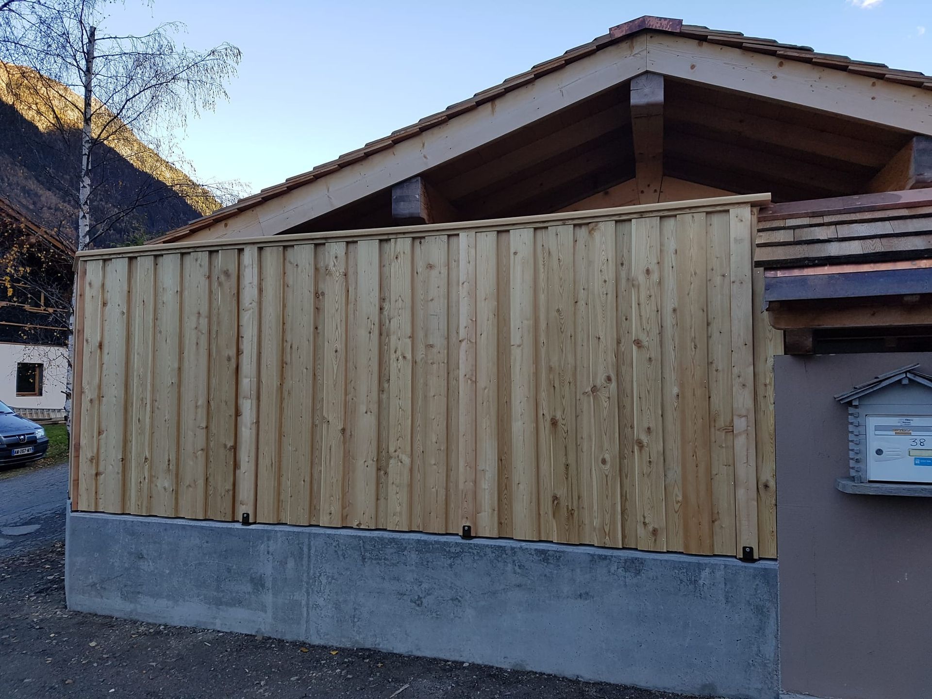 Clôture en bois pour préserver l'intimité, installée au sommet d'un mur en béton, à côté d'une maison au toit en pente.